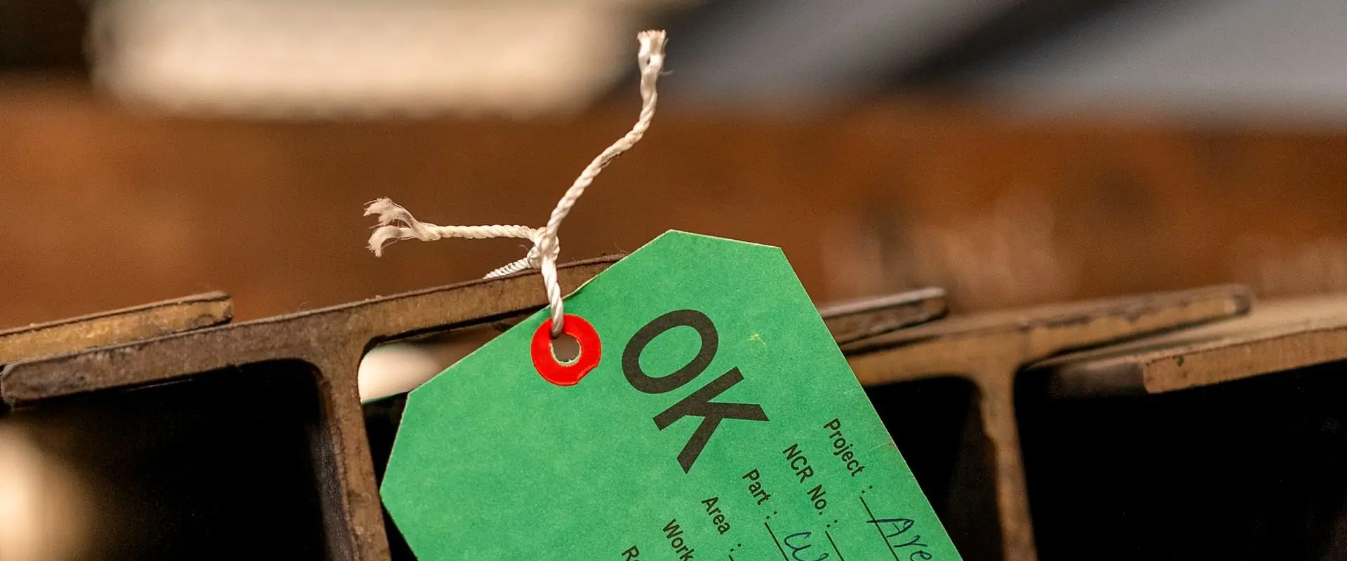 A green inspection tag marked OK, tied to a stack of steel sections.