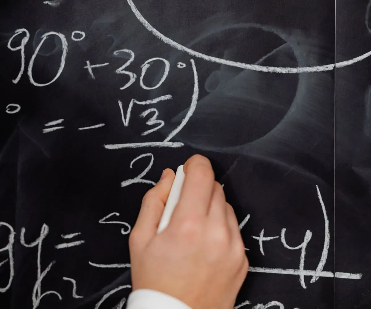 A hand writing a mathematical formula in chalk on a blackboard.