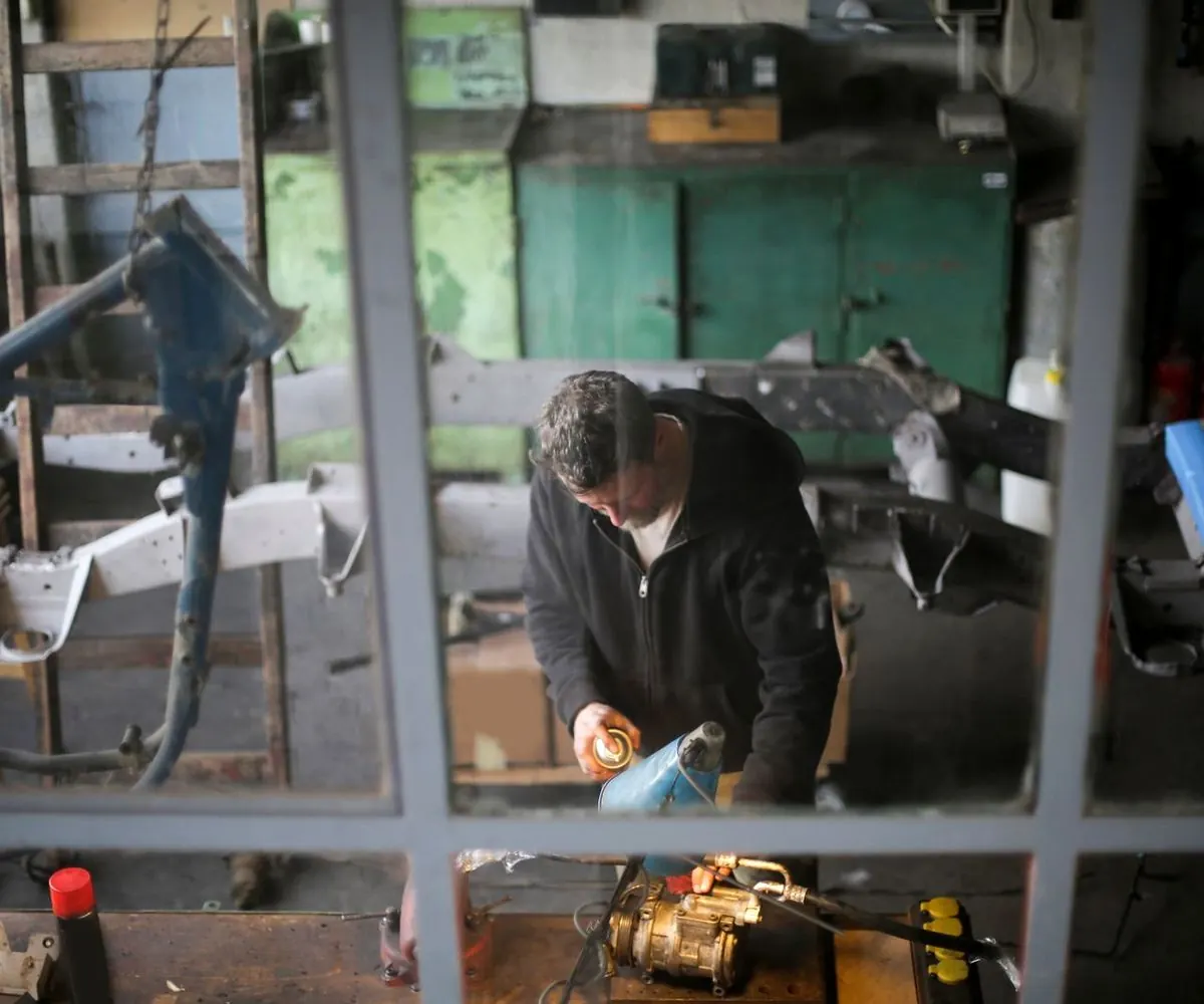 A mechanic bent over metal components on a bench, face out of frame.