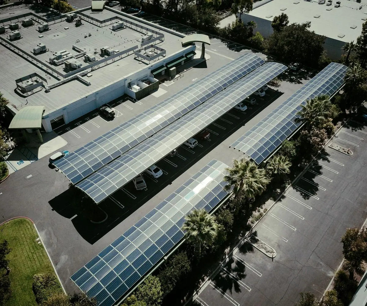 Long canopies of solar panels shading a parking area beside a low industrial building, from the air.