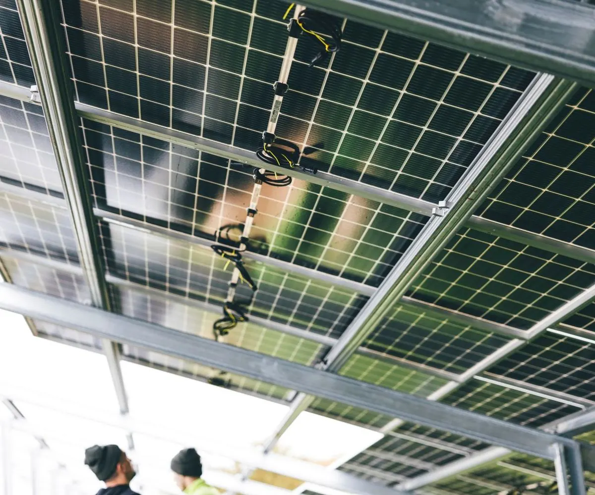 The underside of a solar array, its frame and mounting rails in shadow.