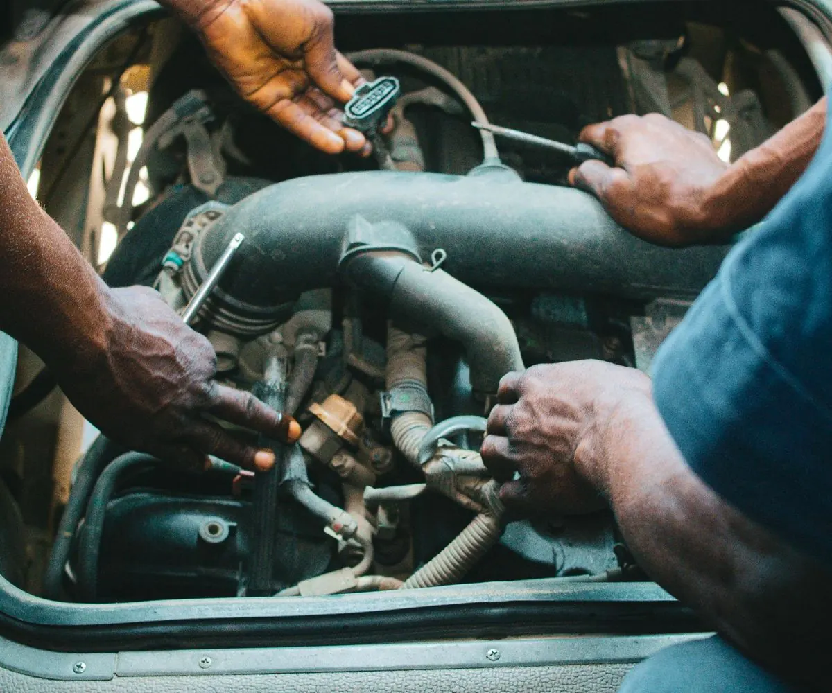 Four hands working together over an open engine bay, tools in use.