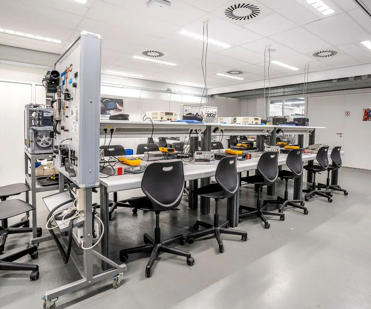 Benches of diagnostic equipment and empty chairs in an automotive training workshop.